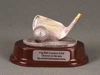 This is a image of a silver colored chipping wedge with a golf ball set on a dark red oval base